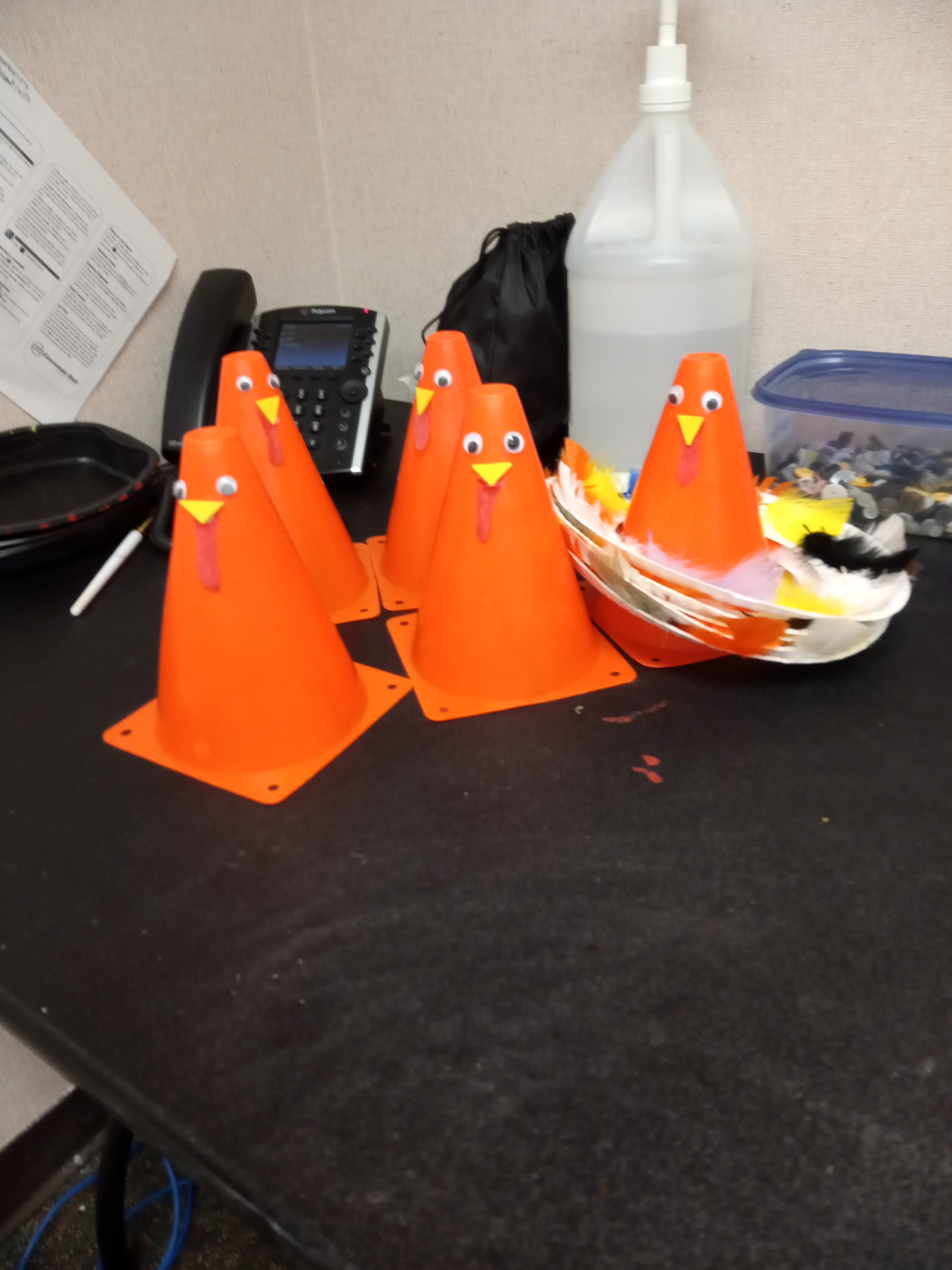 5 small orange pylons with little bird faces on them. One has paper plates with feathers around it.