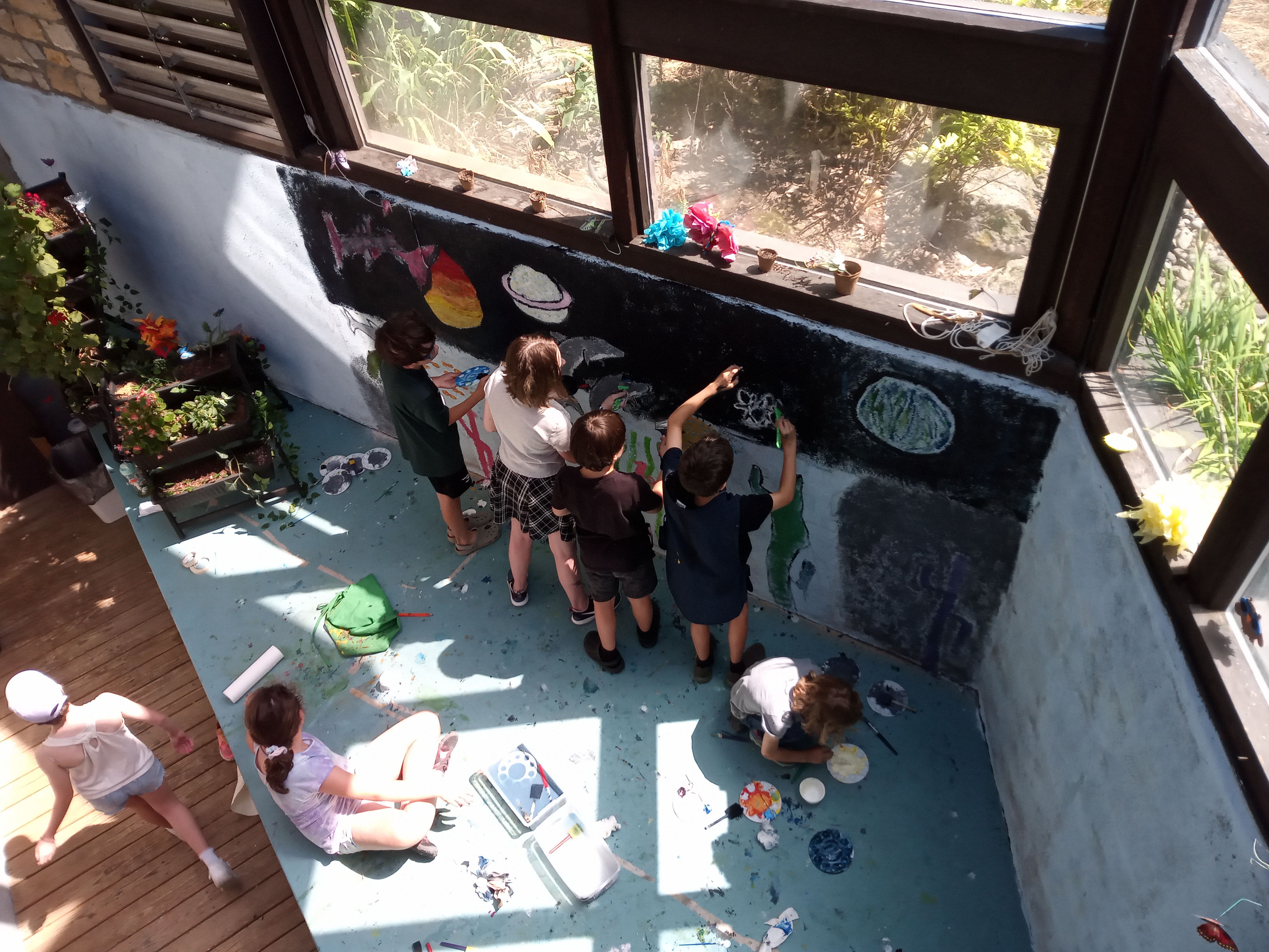 Overhead photo of six children painting a wall together.