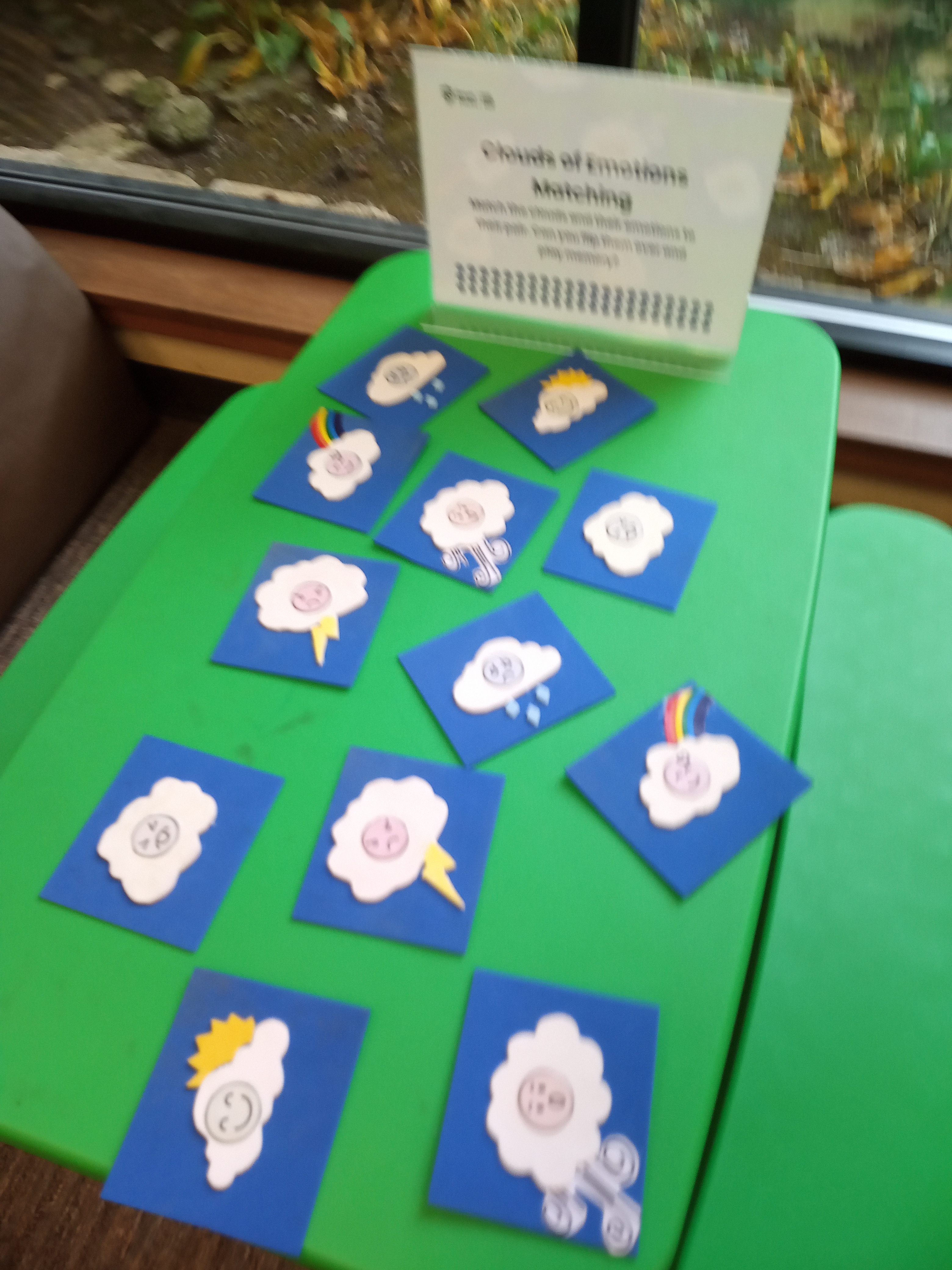 A green table with a dozen blue cards with different clouds that have faces on it.